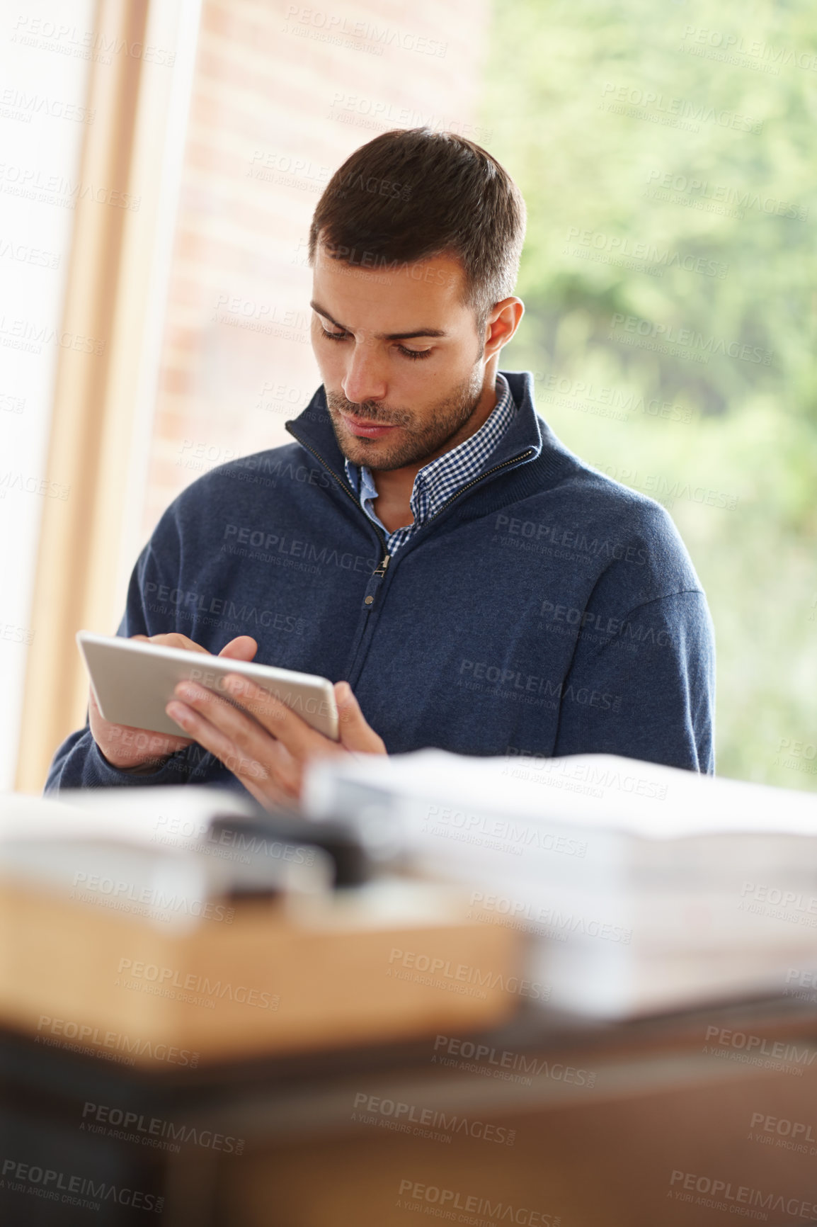 Buy stock photo Shot of a casual young man using a digital tablet at his desk