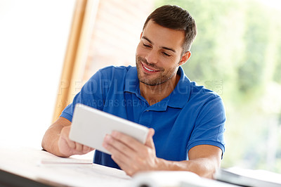 Buy stock photo Shot of a casual young man using a digital tablet at his desk