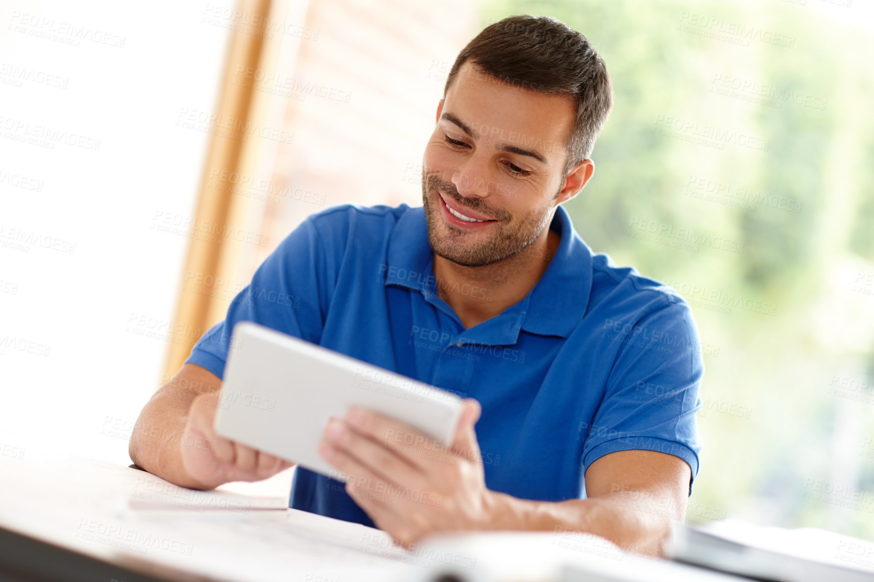 Buy stock photo Shot of a casual young man using a digital tablet at his desk