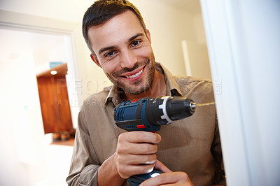 Buy stock photo Portrait of a smiling young man drilling a hole into the wall