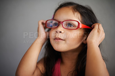 Buy stock photo Little girl wearing glasses to help with vision at an optometry consultation, smiling against grey copyspace background. Child with blurry vision getting fitted with spectacles at an ophthalmologist