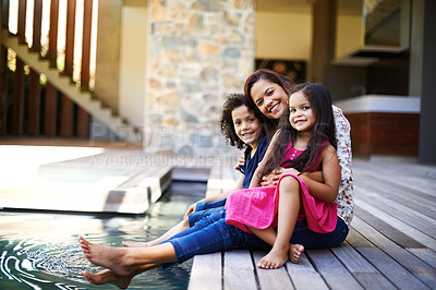 Buy stock photo Shot of a mother with her two children dipping their feet into the pool on the patio
