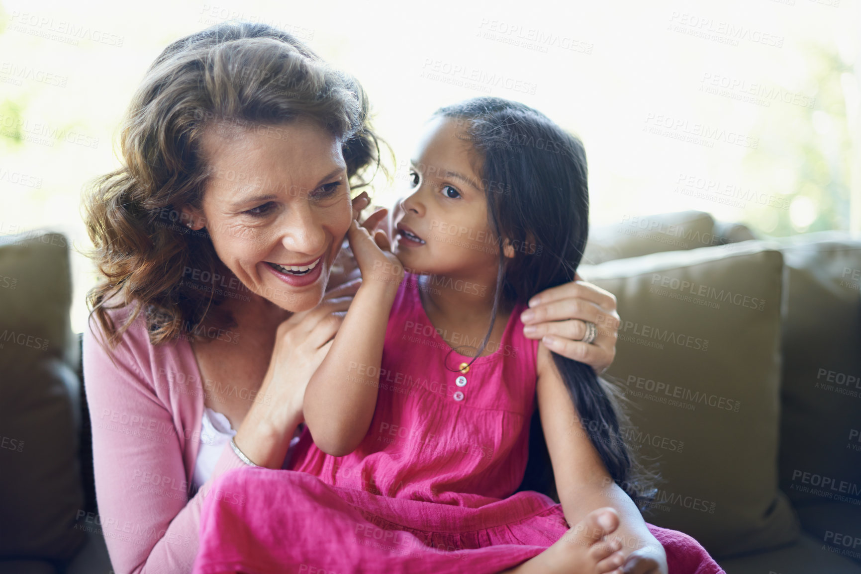 Buy stock photo Grandma, girl and whisper on sofa in home with bonding, support and care for child development. People, kid and smile in couch for memories, fun and growth as family together for love and trust