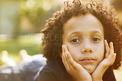 Buy stock photo A solemn little boy lying on the grass with his head in his hands