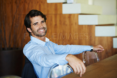 Buy stock photo A laidback young businessman sitting at a table and looking at the camera