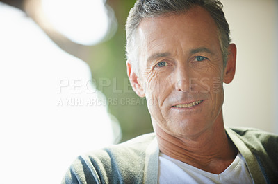 Buy stock photo Closeup portrait of a mature man in casual clothing sitting at home on a sunny day. A handsome senior caucasian man relaxing and smiling at the camera. One retired older man enjoying his free time