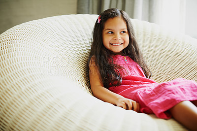 Buy stock photo A cute little girl sitting on a chair at home and looking away