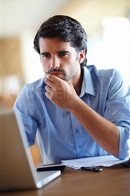 Buy stock photo A thoughtful young businessman working on his laptop at his desk