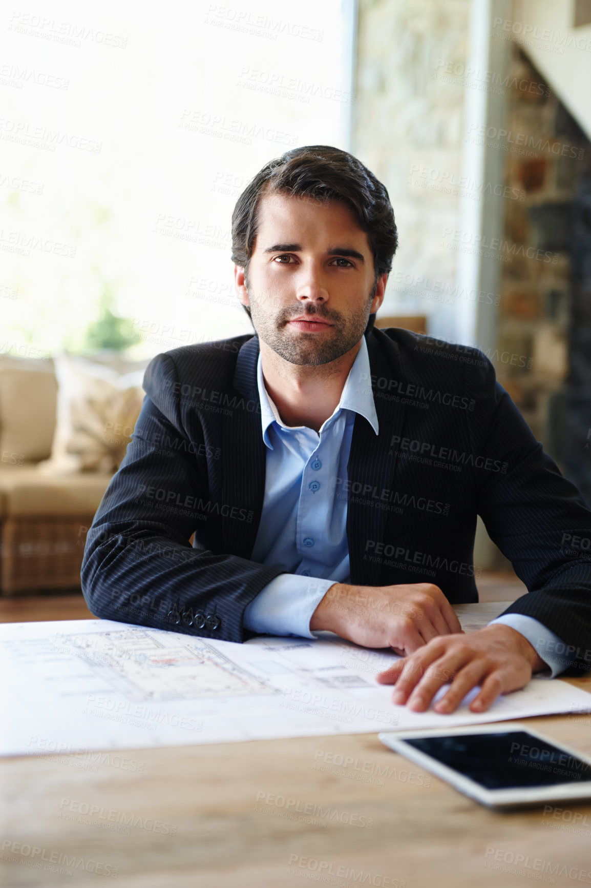 Buy stock photo A young architect sitting at his desk with his floor plans spread out in front of him