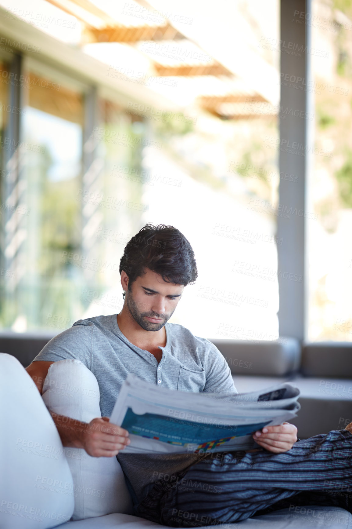 Buy stock photo Home, man and newspaper for reading on couch in living room for information, story or news. House, lounge and male reader with article on vacation, holiday and weekend trip in London to relax on sofa