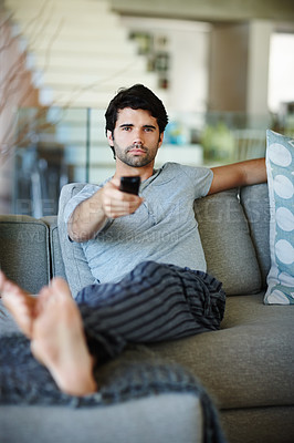 Buy stock photo Portrait of a man watching TV and holding a remote. A young male relaxed on a couch at home and focused on a show. Person cozy and comfortable on a sofa enjoying some entertainment