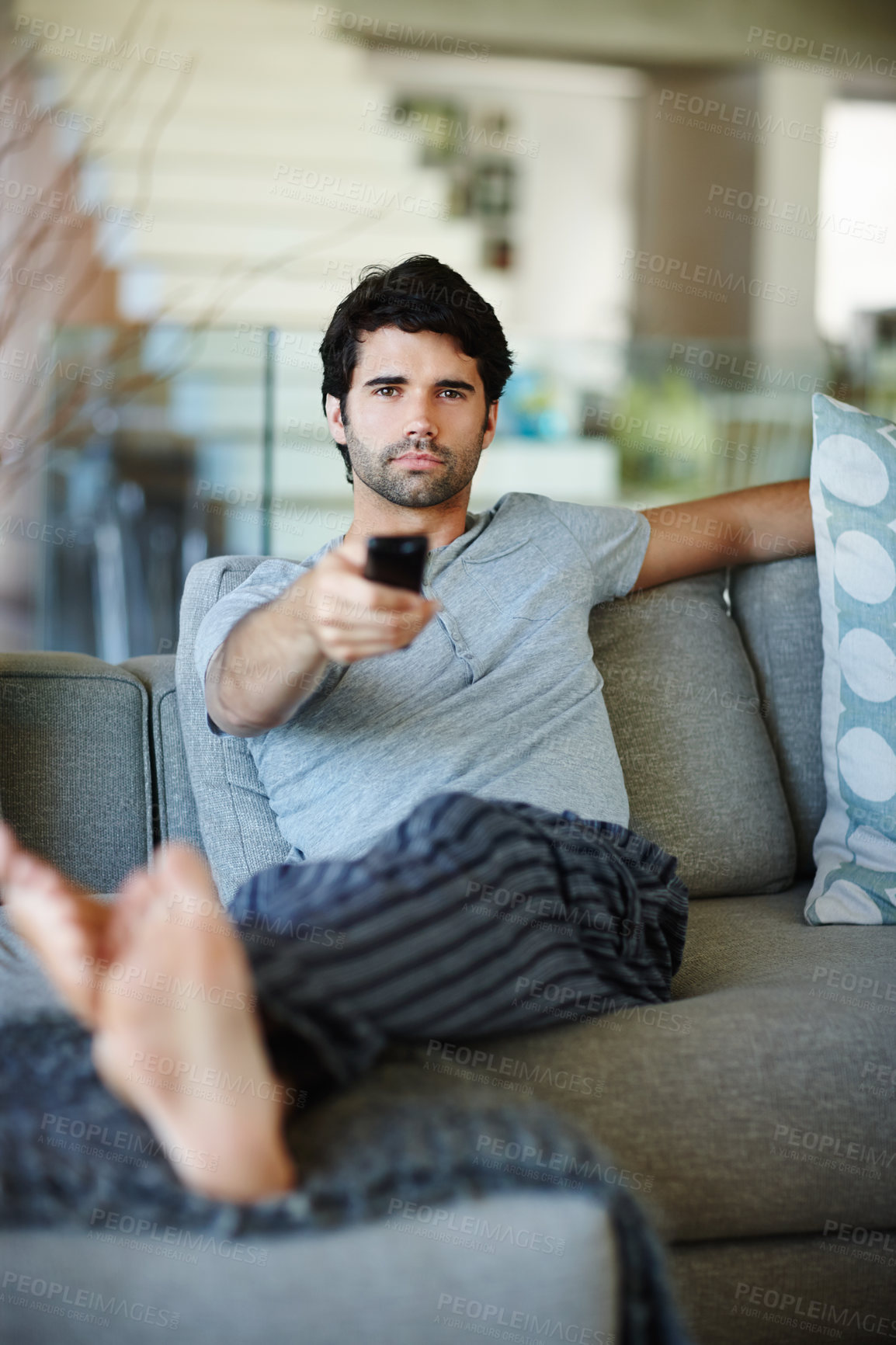 Buy stock photo Portrait of a man watching TV and holding a remote. A young male relaxed on a couch at home and focused on a show. Person cozy and comfortable on a sofa enjoying some entertainment