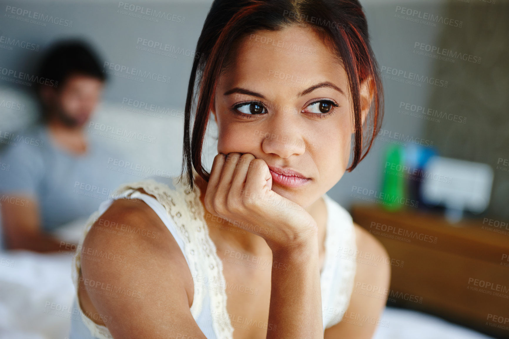 Buy stock photo Shot of an upset woman sitting on the side of her bed with her boyfriend in the background