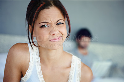 Buy stock photo Portrait of a woman scrunching up her face sitting in her bedroom with her boyfriend in the background