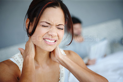 Buy stock photo Shot of a woman sitting on the side of her bed with bad neckache with her boyfriend in the background