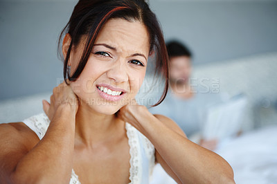 Buy stock photo Shot of a woman sitting on the side of her bed with bad neckache with her boyfriend in the background