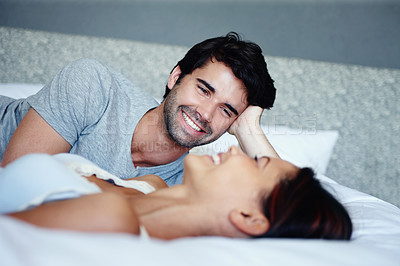 Buy stock photo Shot of a smiling couple lying in bed and talking