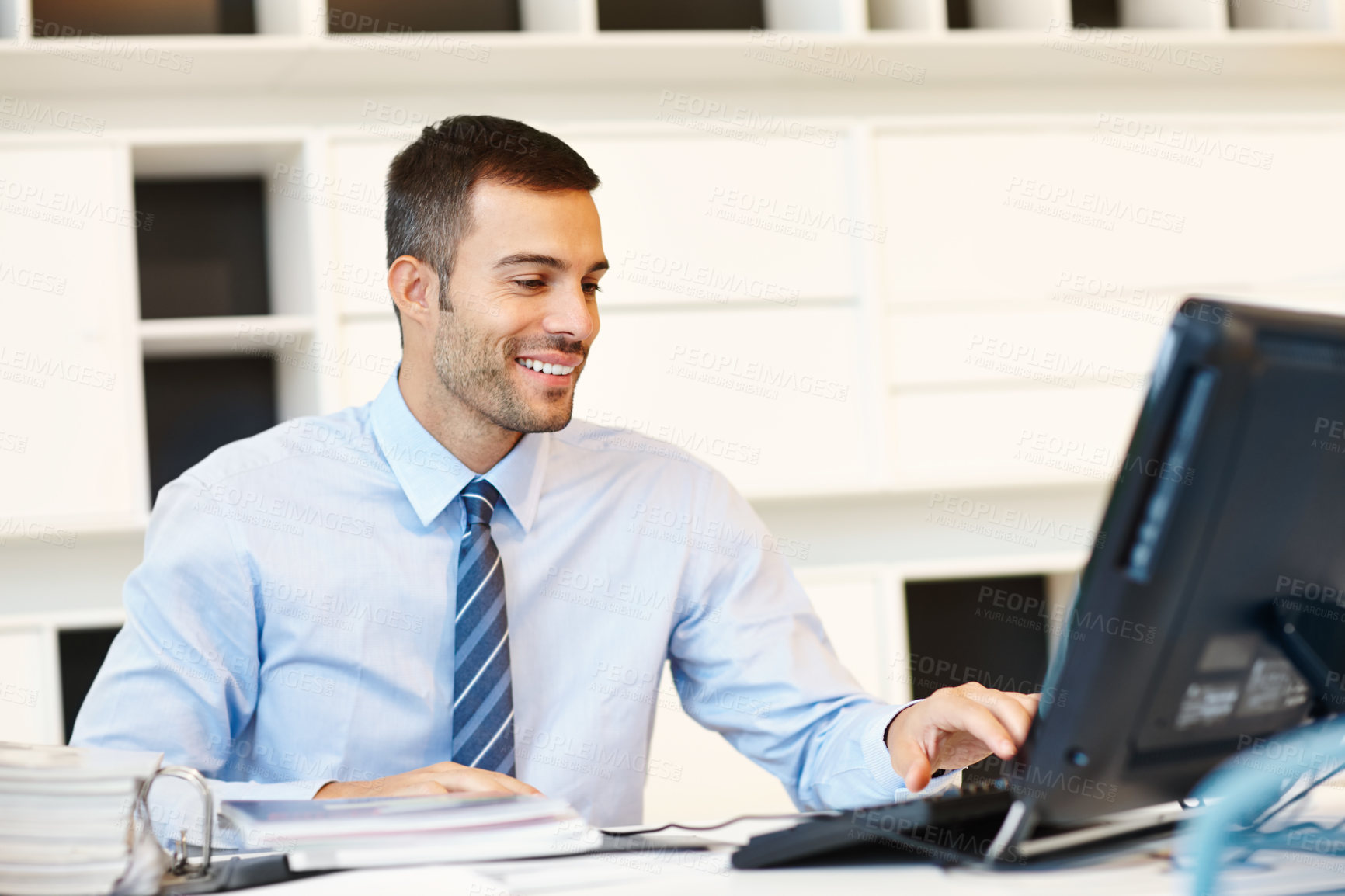 Buy stock photo Young handsome businessman using a desktop computer  at his desk in an office at work. One happy male businessperson using a pc sitting at a table. Business professional typing an email