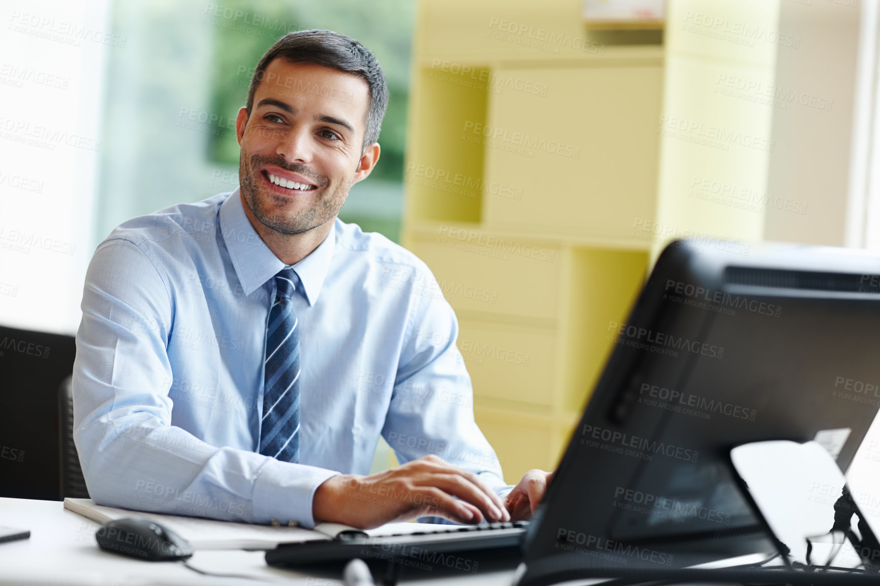 Buy stock photo A smiling young businessman sitting at his desk and working