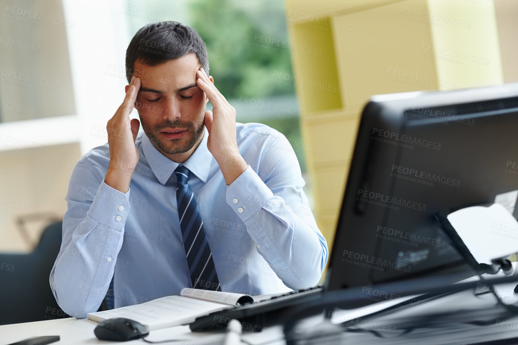 Buy stock photo A stressed young businessman sitting at his desk and struggling with a bad headache