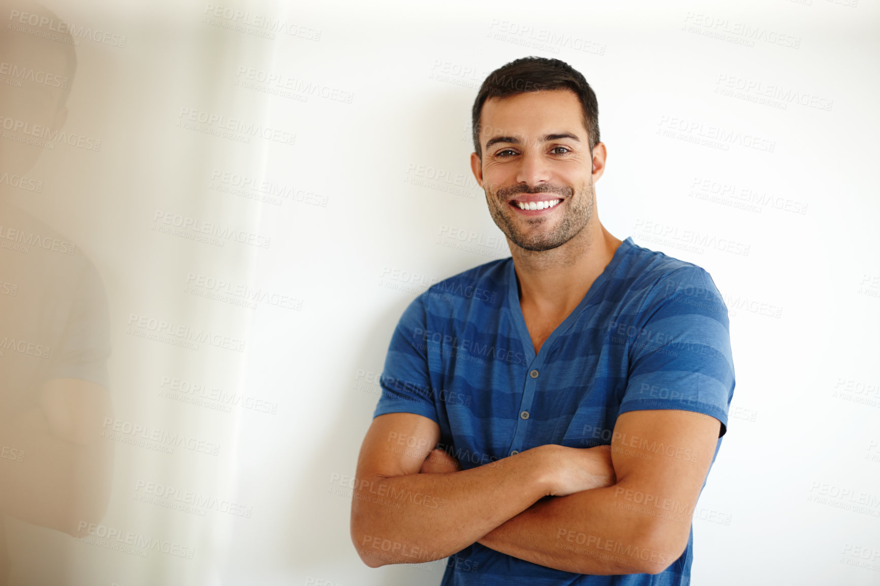 Buy stock photo Trendy, proud young man with his arms crossed leaning against a white wall. Portrait of confident, stylish handsome man with his arms folded. Relaxed posing against a studio background 



