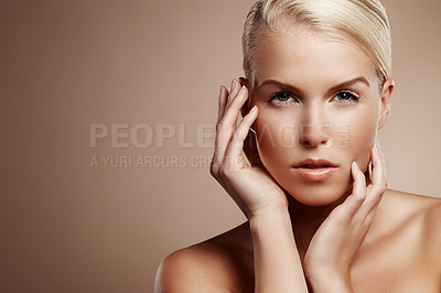 Buy stock photo Portrait of a beautiful blonde woman touching her face, isolated on brown beige background. One young female model with flawless, clear skin standing in a studio for beauty, skincare concept