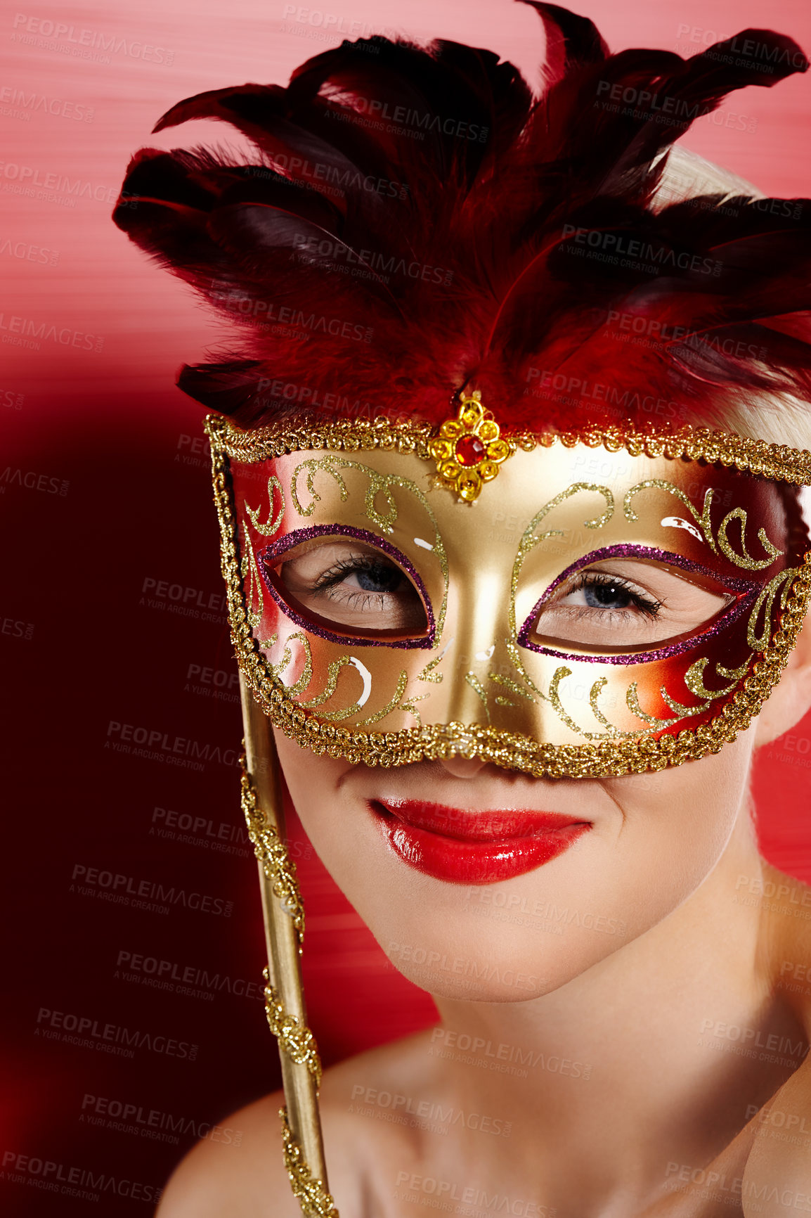 Buy stock photo Portrait, happy and woman in carnival mask for fun, art deco and dress up by red background. Smile, pride and female person with mysterious or playful look for cosplay in studio with lipstick