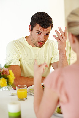 Buy stock photo A frustrated man gesturing while having an argument with his wife across the dinner table