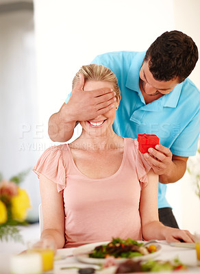 Buy stock photo A handsome man covering his girlfriend's eyes from behind while he hands her a ring box