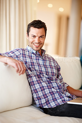 Buy stock photo A handsome man smiling at the camera while relaxing on a sofa at home