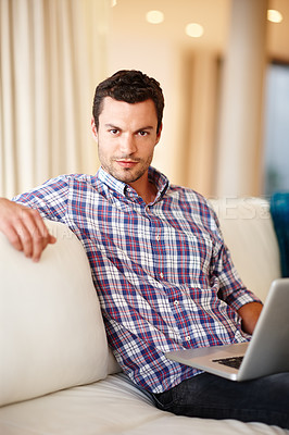 Buy stock photo A handsome man smiling at the camera while sitting on the couch with his laptop