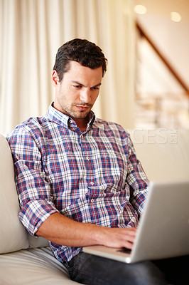 Buy stock photo A handsome sitting on a couch working on his laptop
