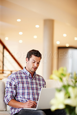 Buy stock photo A handsome man sitting on his couch at home working on his laptop