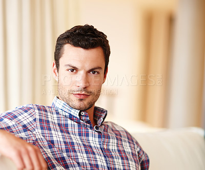 Buy stock photo A handsome man smiling at the camera while relaxing on his couch