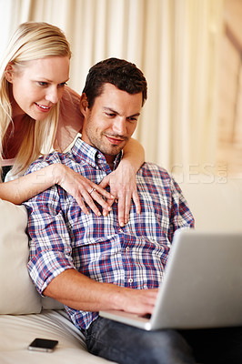 Buy stock photo A beautiful woman hugging her husband from behind while he sits on the couch working on his laptop