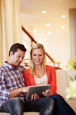 Buy stock photo A happy couple sitting on their couch working on a digital tablet - copyspace