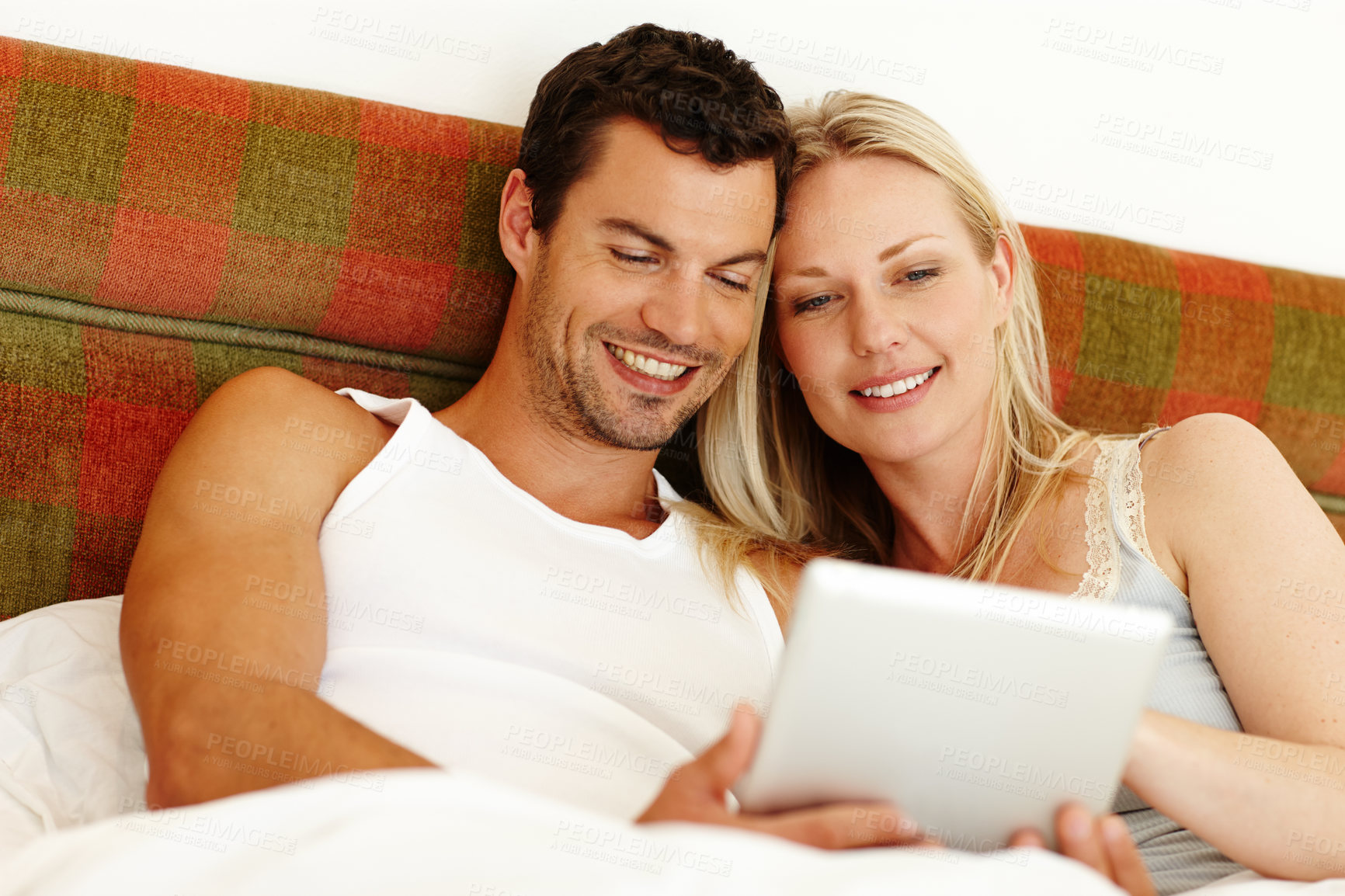 Buy stock photo An attractive young couple sharing a digital tablet while relaxing in bed at home