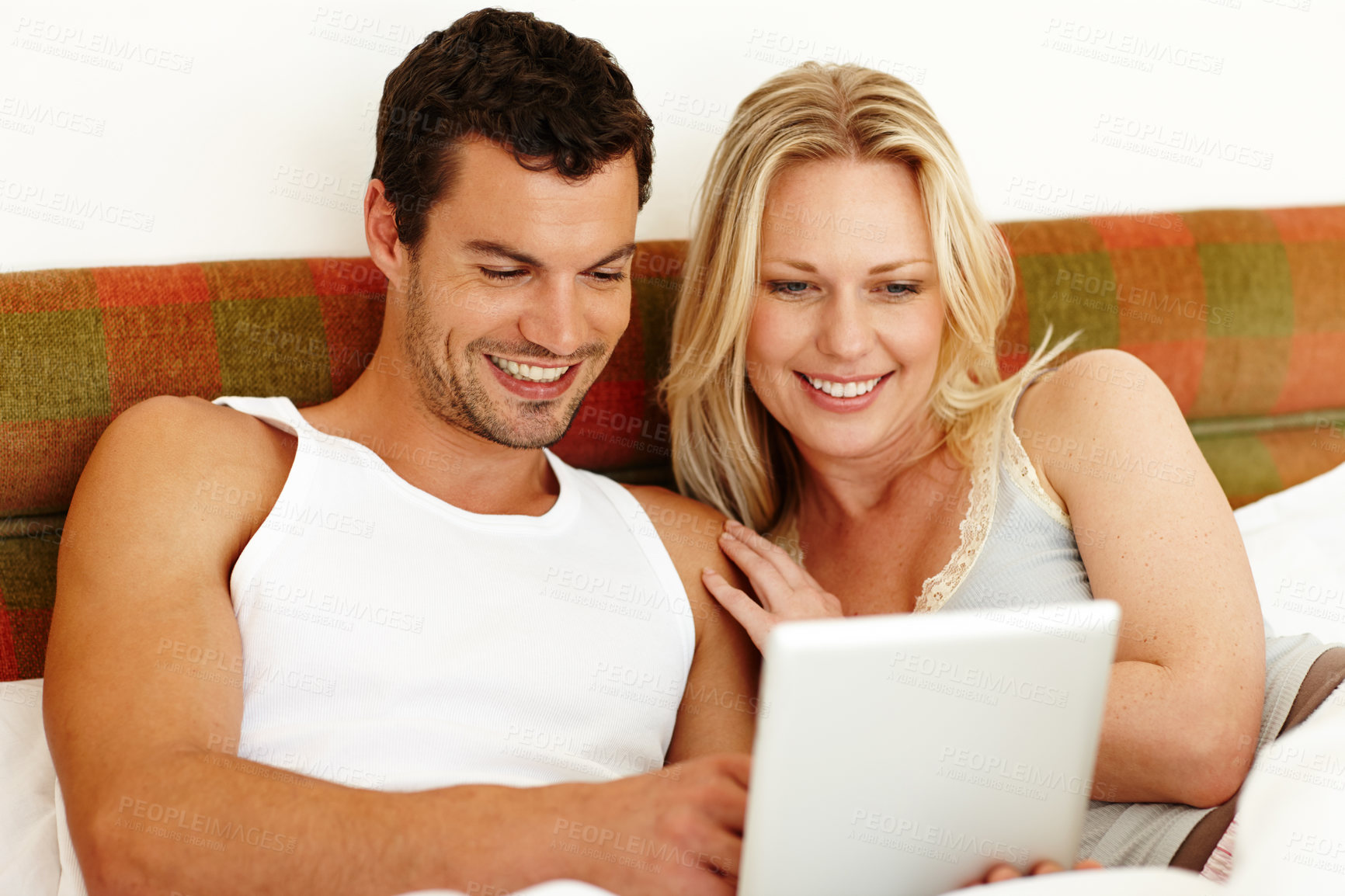 Buy stock photo An attractive young couple sharing a digital tablet while relaxing in bed at home