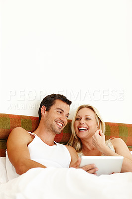 Buy stock photo An attractive young couple sharing a digital tablet while relaxing in bed at home