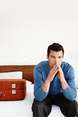 Buy stock photo A pensive young man sitting on his bed alongside a suitcase