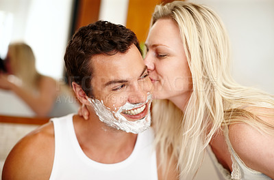 Buy stock photo A handsome happy man with shaving cream on his face with his girlfriend kissing his cheek