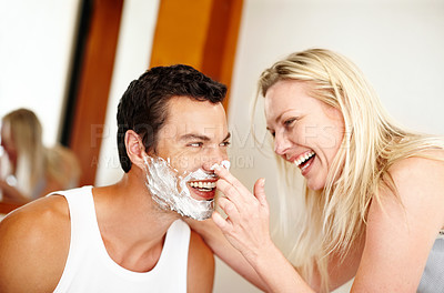 Buy stock photo Shot of a young woman putting shaving cream on her husband and laughing