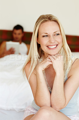 Buy stock photo Portrait of pretty woman sitting at the edge of the bed with her boyfriend lying in the background