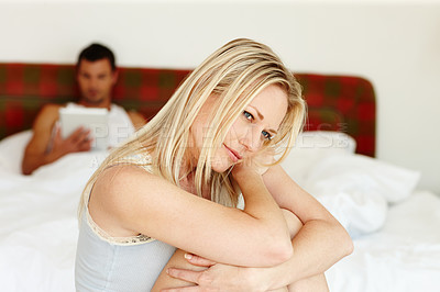 Buy stock photo Portrait of a vulnerable looking woman sitting at the edge of the bed with her boyfriend lying in the background