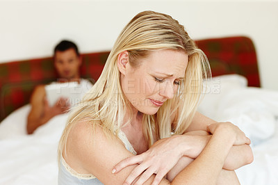 Buy stock photo An upset woman sitting on the edge of her bed while her husband lying in the background