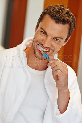 Buy stock photo A handsome man in a bathrobe smiling at the camera while he holds a toothbrush
