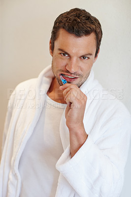Buy stock photo A handsome man in a bathrobe smiling at the camera while he holds a toothbrush
