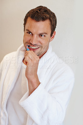 Buy stock photo A handsome man in a bathrobe smiling as he brushes his teeth
