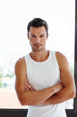 Buy stock photo A handsome man standing with his arms folded in front of his window