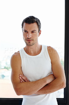 Buy stock photo A handsome man standing with his arms folded in front of his window